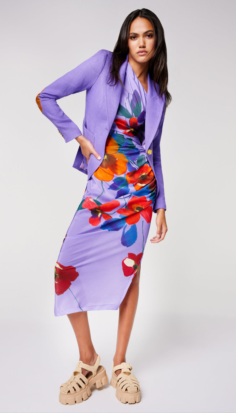 A woman in a solid purple blazer layered over a floral dress.