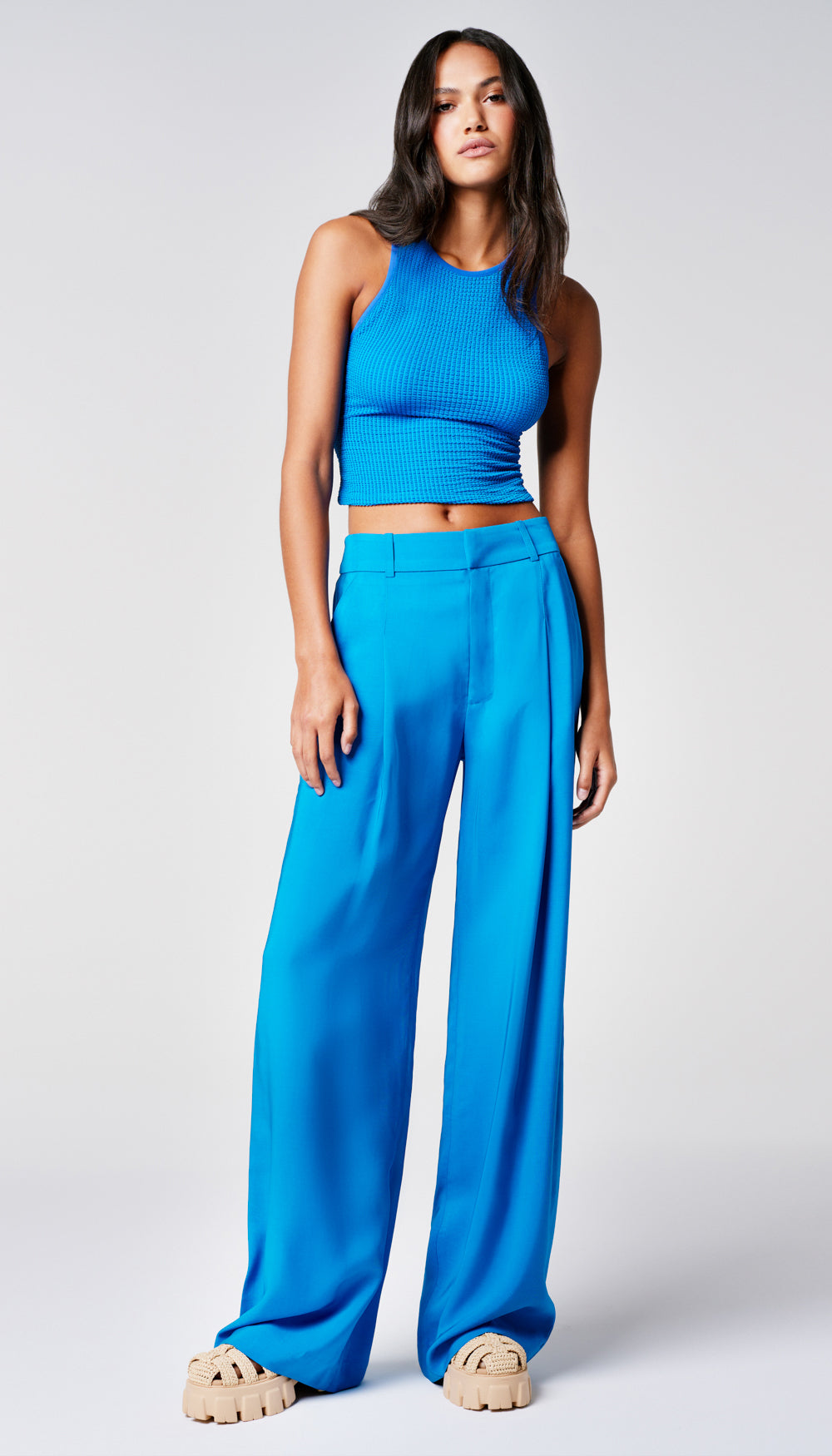 A woman in a solid blue tank and wide leg trousers.