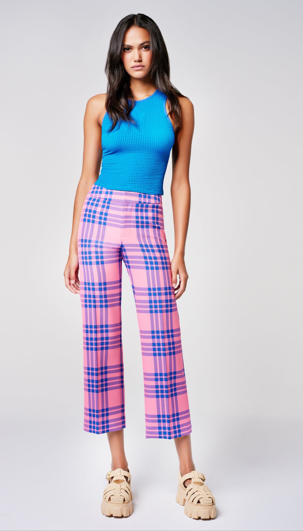 A woman in a pink and blue plaid pant and solid blue tank.